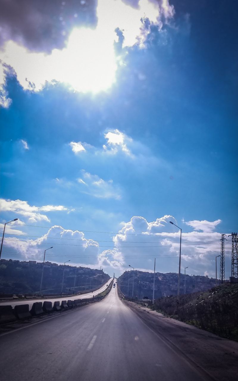 a road with power lines on the side and blue sky with clouds